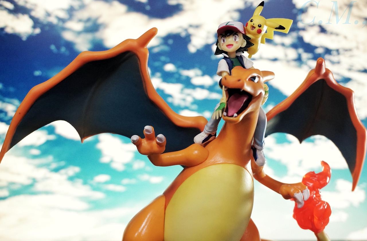 Figurines of Ash Ketchum and Pikachu riding on Charizard against a blue sky with clouds.