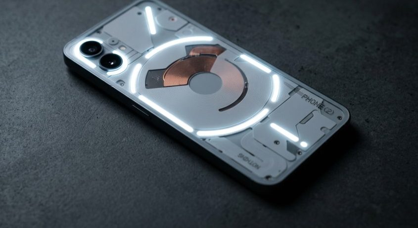 Close-up of Nothing Phone (2) transparent back with illuminated Glyph lights on a dark surface.